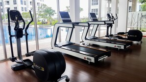 Un gimnasio con cintas de correr, una elíptica y una máquina de remo, con amplios ventanales que dan a una piscina y edificios.