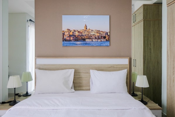A hotel room with a bed, two bedside lamps, a headboard, and a cityscape painting on the wall.