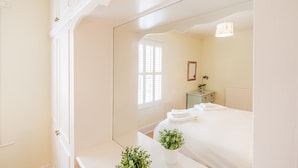 A bedroom with a large mirror, a bed with neatly folded white towels, a small bedside table with a lamp, and a window with shutters. - Strayside Cottage Harrogate. Dog friendly. 5 min walk hospital. 15 min walk town (Harrogate)