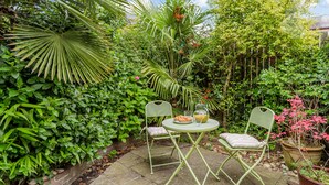 A small outdoor garden with a table and two chairs, surrounded by lush greenery and a variety of plants. - Strayside Cottage Harrogate. Dog friendly. 5 min walk hospital. 15 min walk town (Harrogate)