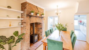 A dining area with a brick fireplace, green upholstered chairs, and a wooden table. - Strayside Cottage Harrogate. Dog friendly. 5 min walk hospital. 15 min walk town (Harrogate)