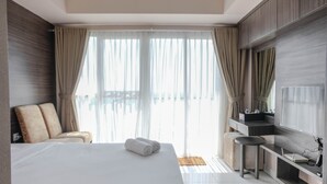 A modern hotel room with a large bed, a seating area with a sofa and armchairs, a small table, a TV, and a balcony view.