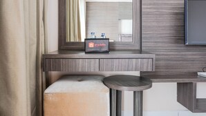 A hotel room with a wooden vanity, a round table, a bench, and a minibar with a travelio sign.