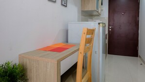 Una habitación pequeña y limpia con un escritorio de madera, una silla, un refrigerador y una puerta.