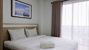 Una cama bien hecha con ropa de cama blanca, un cuadro enmarcado de un paisaje urbano en la pared y una ventana con cortinas translúcidas.