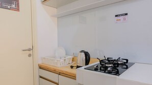 Une petite cuisine équipée d’une cuisinière à gaz, d’une bouilloire et d’une machine à café. On y trouve une porte blanche avec une poignée et une petite fenêtre sur laquelle est apposée une pancarte.