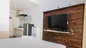 Une chambre d’hôtel moderne avec un grand lit, un téléviseur à écran plat fixé à un mur en bois, une kitchenette équipée d’un réfrigérateur et d’une cuisinière, et une petite fenêtre.