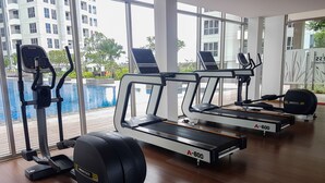 Une salle de sport équipée de tapis de course, d’un vélo elliptique et d’un rameur, donnant sur une piscine et un immeuble doté de balcons.