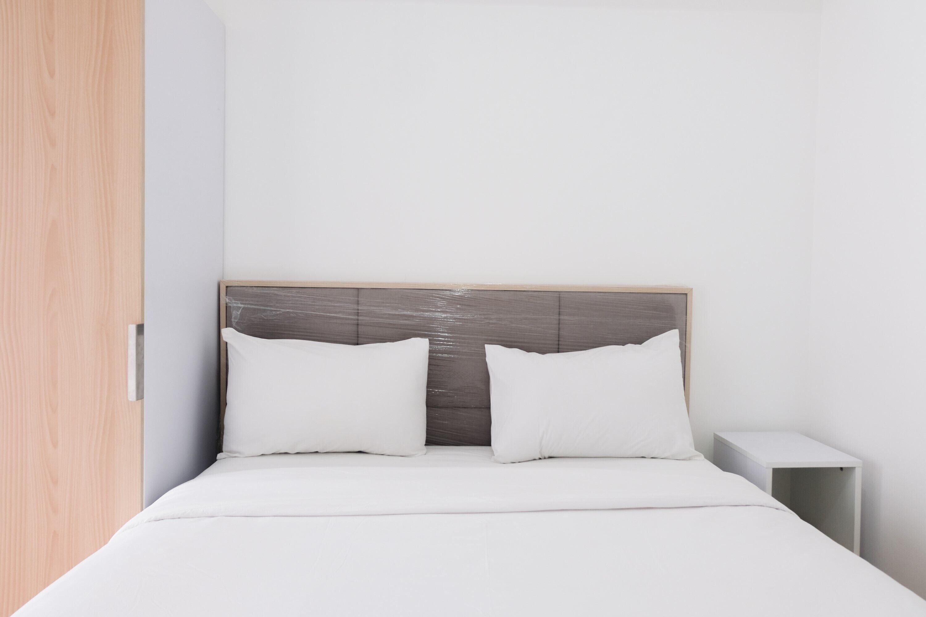 A bedroom with a bed, two pillows, a nightstand, and a wooden wardrobe.