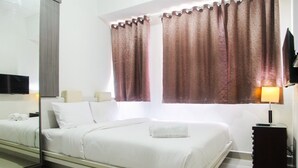 A hotel room with a large bed, a bedside table with a lamp, and a mirror reflecting the room. - 1BR with Working Space The Oasis Apartment Cikarang (Cikarang)