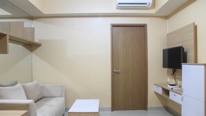A modern room with a wooden door, a white sofa, a small white table, a TV on a wooden stand, and a white cabinet. - Spacious 1 BR at The Oasis Cikarang Apartment (Cikarang)
