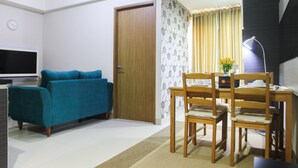 A living room with a teal sofa, wooden dining table, and chairs, a TV, and a door.