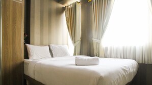 A neatly made bed with white linens and a folded towel, a wooden wardrobe, and a window with curtains.