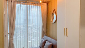 A room with a large window, a sofa, a small table with a plant, and a hanging light fixture.