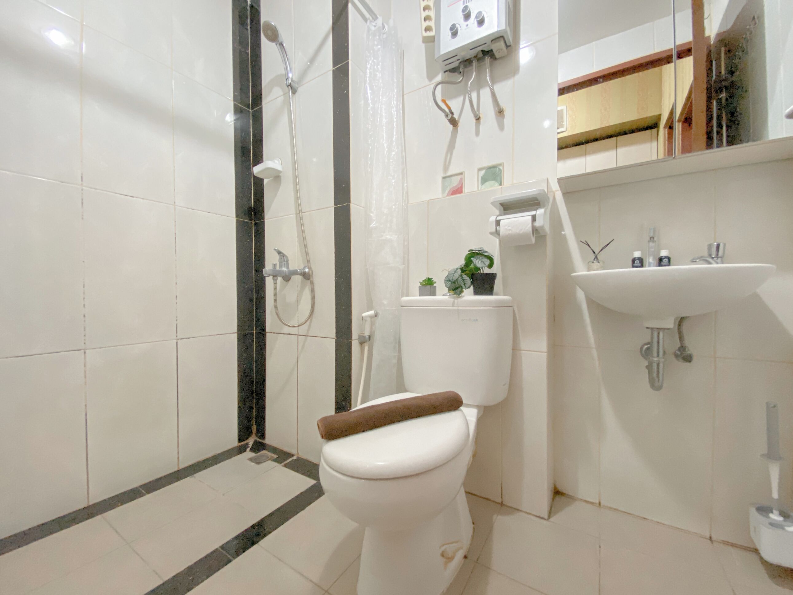 A bathroom with a toilet, shower, sink, and a toilet paper holder.