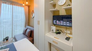A modern hotel room with a large bed, a sofa, a desk with a computer, a TV, and a window with curtains.