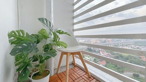A balcony with a potted monstera plant and a white chair, overlooking a cityscape.