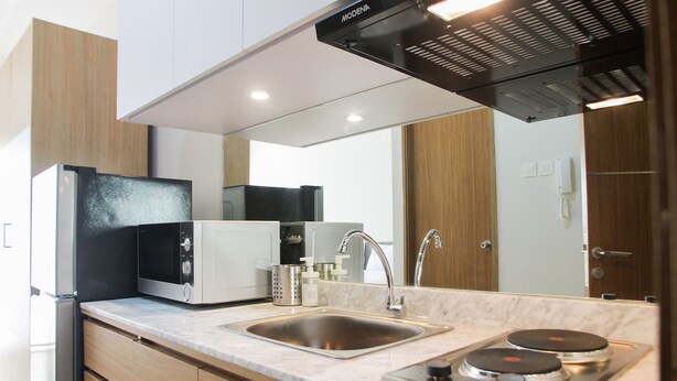 A modern kitchen with a built-in microwave, stainless steel sink, and a gas stove. - Comfy Studio Room @ Oasis Apartment (Cikarang)