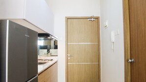A compact kitchen with a refrigerator, wooden cabinets, and a door. - Comfy Studio Room @ Oasis Apartment (Cikarang)