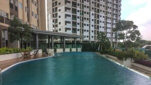 A swimming pool with a lounge area, surrounded by a high-rise building with multiple balconies. - Comfy Studio Room @ Oasis Apartment (Cikarang)