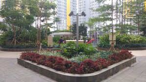 A landscaped urban area with a central garden, a playground, and a tall residential building in the background. - Exclusive 2BR Springlake Summarecon Bekasi Apartment (Bekasi)