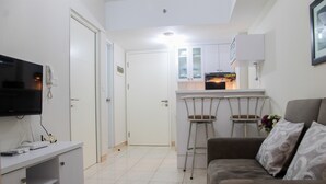 A modern living room with a flat-screen TV, a sofa, and a coffee table. There is a kitchen area with a fridge, oven, and bar stools. - Exclusive 2BR Springlake Summarecon Bekasi Apartment (Bekasi)
