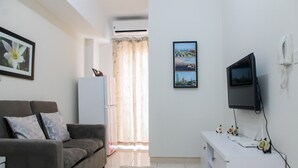 A living room with a sofa, a flat-screen TV, a white cabinet, and a framed cityscape picture on the wall. - Exclusive 2BR Springlake Summarecon Bekasi Apartment (Bekasi)