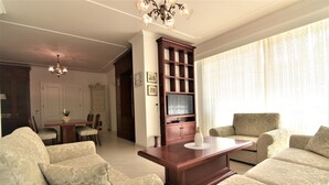 A living room with a sofa set, a wooden coffee table, a television, and a chandelier. - Vila Ključe Apartmnets (Bled)