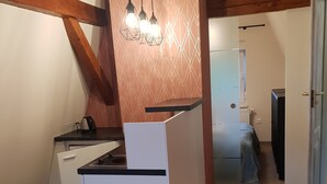 A compact kitchen with a built-in refrigerator, a stove, and a sink. There is a wooden beam ceiling and a patterned wall above the kitchen. - Willa Azalia (Polanica-Zdroj)