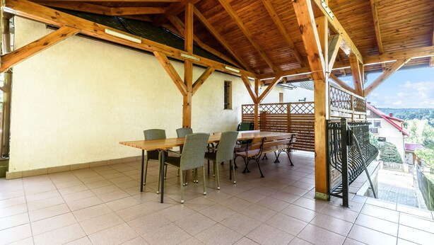 An outdoor patio with wooden beams, a table with chairs, and a view of the surrounding landscape. - Willa Azalia (Polanica-Zdroj)