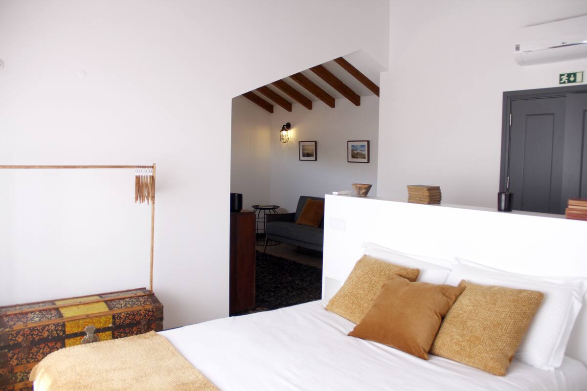 Une chambre d’hôtel avec un lit, une tête de lit en bois, une petite table et un canapé à l’arrière-plan.