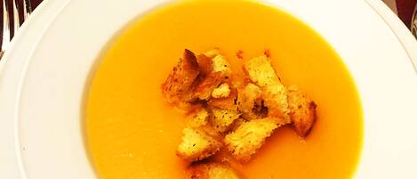 A white plate with a bowl of soup and croutons on a table.