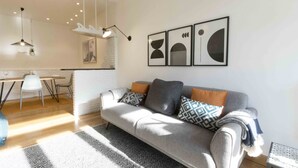 Een moderne woonkamer met een grijze bank, een getextureerd vloerkleed en abstracte wandkunst.