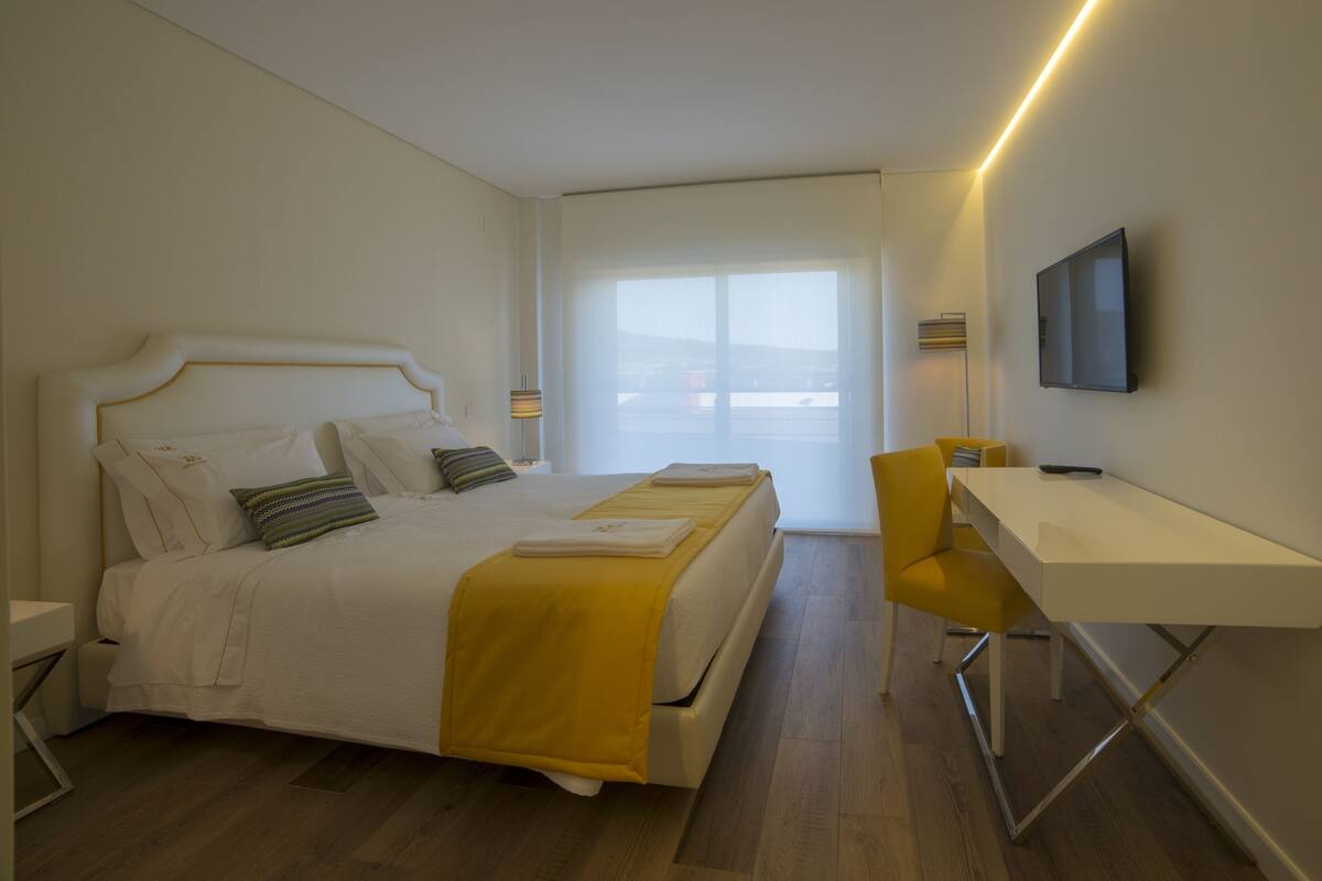 A hotel room with a bed, a desk, a chair, a TV, and a window with a view.