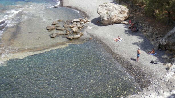 Una playa con agua cristalina, piedras y rocas.
