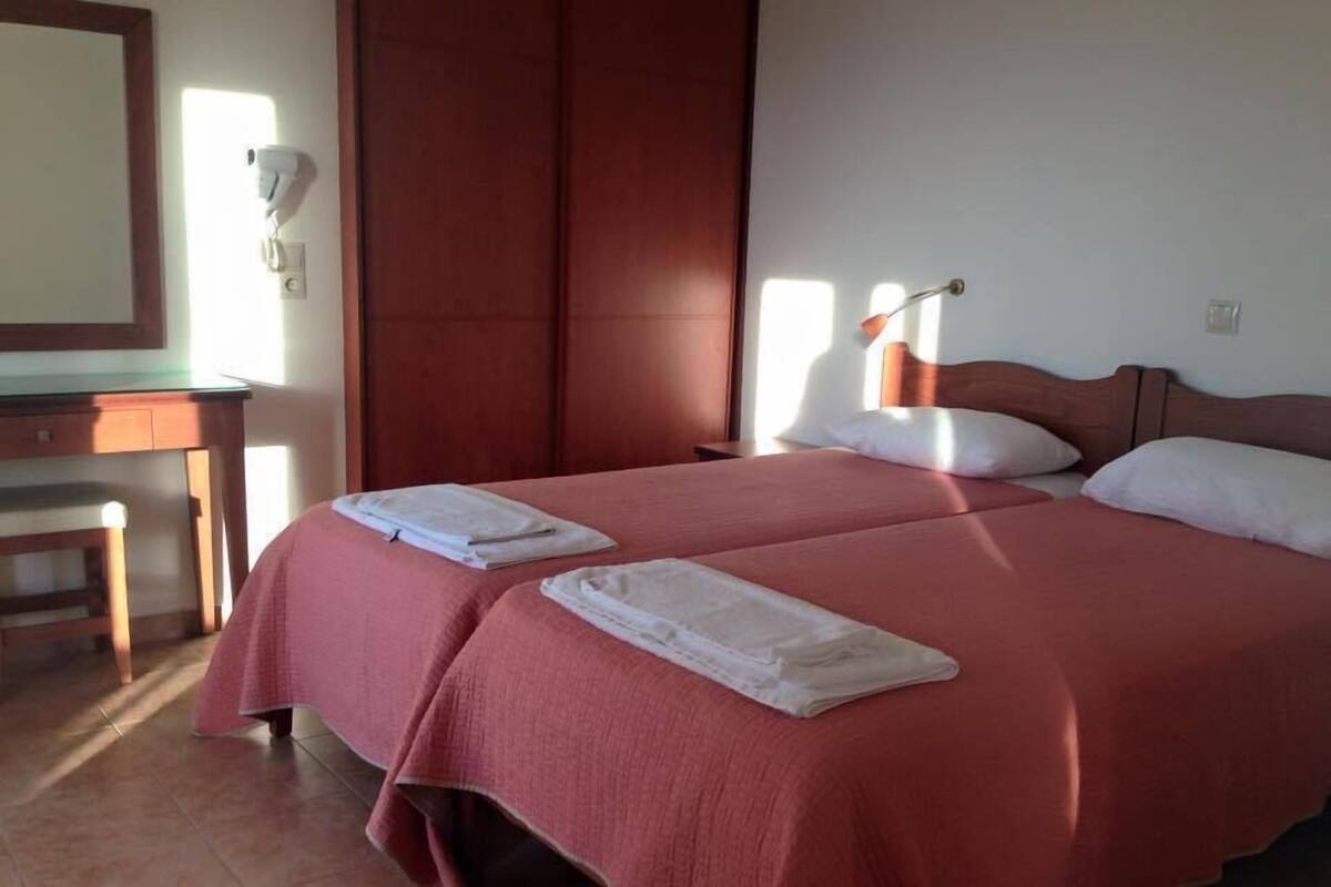 Una habitación de hotel con cama, dos almohadas, mesita de noche, lámpara y espejo.
