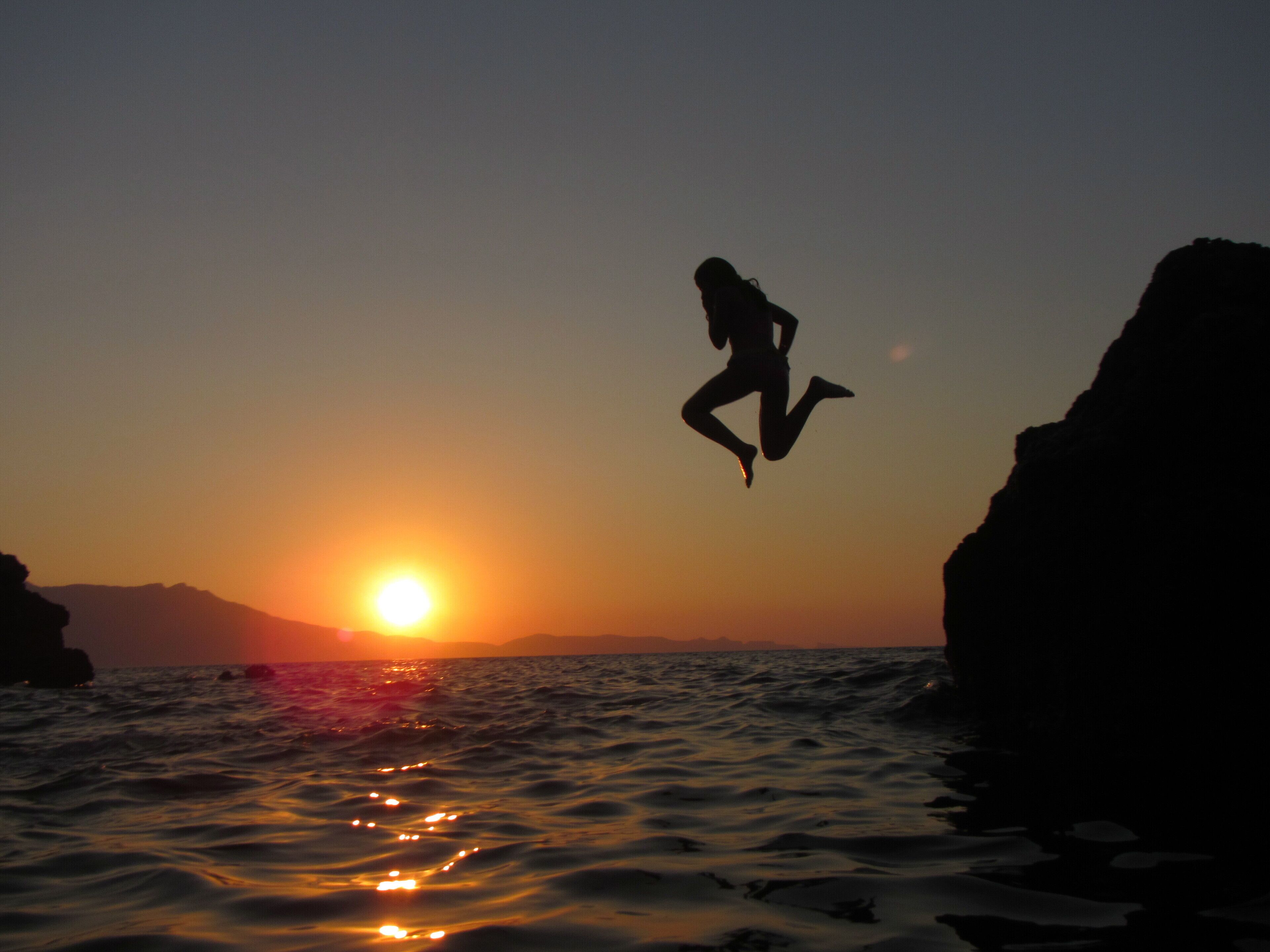 A silhouette of a person jumping into the ocean at sunset.