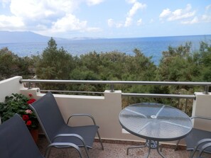 A balcony with a table and chairs, overlooking a body of water and distant mountains. - Ravdoucha Beach Studios (Platanias)