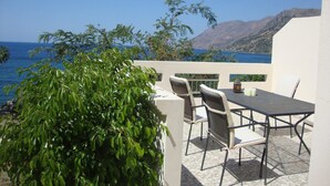 Un patio al aire libre con una mesa y sillas, con vistas a la costa y montañas al fondo.