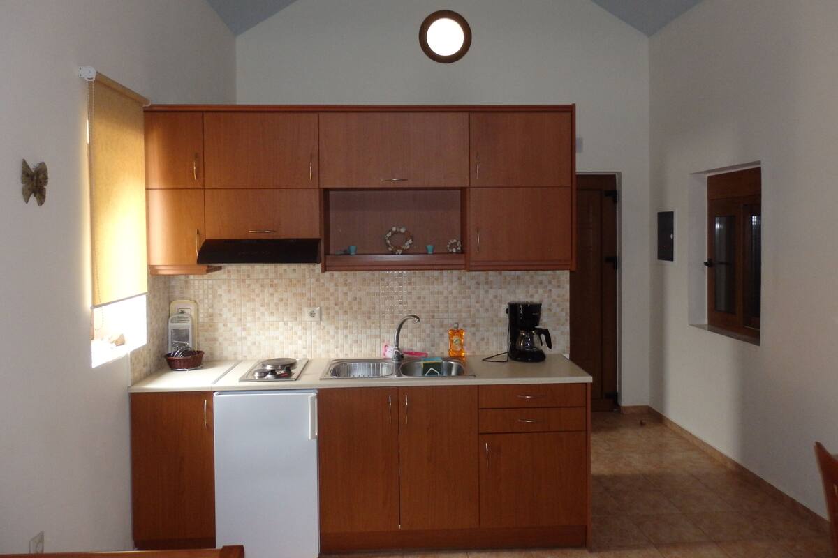 Una cocina compacta con armarios de madera, un refrigerador blanco, un lavamanos y una cafetera.