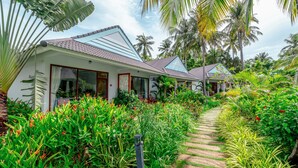 A bungalow with a tiled roof, surrounded by lush greenery and palm trees. - Kingo Retreat Resort (Phu Quoc)