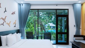 A modern bedroom with a large bed, a seating area, and a view of a garden and pool. - Kingo Retreat Resort (Phu Quoc)