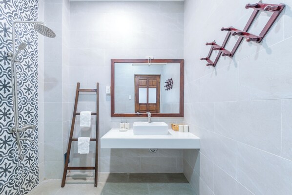 Un bany amb un lavabo blanc, una escala de fusta, un mirall i una dutxera.