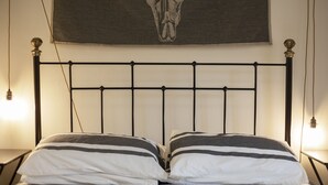 A bed with a metal frame and two pillows, a wall-mounted light, and a skull tapestry. - Old Town Grade II Listed 2 Bed (Margate)