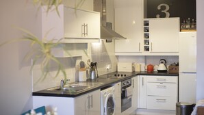 A compact kitchen with white cabinets, a stainless steel range hood, a washing machine, and a small oven. - Old Town Grade II Listed 2 Bed (Margate)