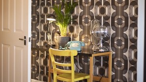 A room with a patterned wallpaper, a closed door, a table with chairs, a potted plant, and a fan. - Old Town Grade II Listed 2 Bed (Margate)
