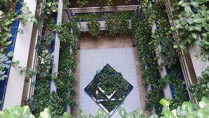 Un atrio de varios niveles con abundante vegetación, incluyendo hiedras y árboles pequeños, y un diseño geométrico de azulejos en las paredes.