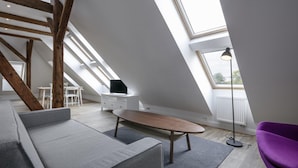 A modern loft bedroom with skylights, a wooden beam structure, a gray sofa, a purple chair, and a small white dresser. - Pytloun Flat Hotel (Liberec)