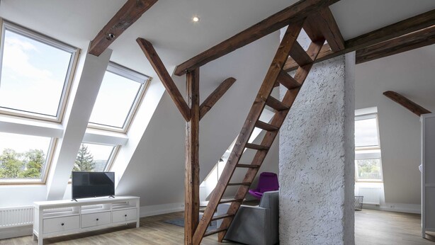 A loft bedroom with exposed wooden beams, a slanted ceiling, and a built-in bench. - Pytloun Flat Hotel (Liberec)