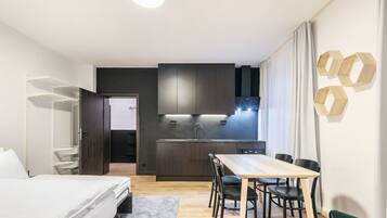 Una habitación de hotel moderna con cama, escritorio, silla, kitchenette y armario.